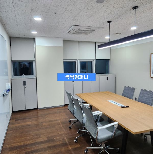 청결하게 관리된 회의실 내부로, 나무 테이블과 여러 개의 회의용 의자가 배치되어 있고 벽면에는 수납공간이 있습니다.